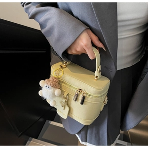 Detail of beige lychee grain leather box bag with gold zippers and cute plush monster charm
