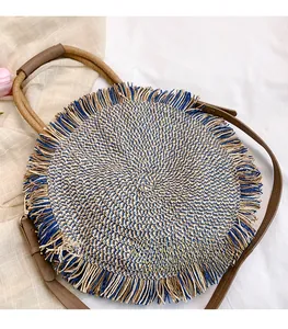Detail of round woven straw bag featuring navy blue tassels and brown leather handles