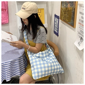 Blue and white plaid canvas tote bag worn by a model in a casual cafe setting