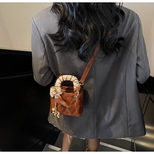 Detail of dark brown quilted handbag with silk scarf handle and pearl charm on a grey suit