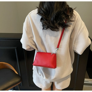Détail du sac seau rouge à texture litchi porté sur une tenue gaufrée grise