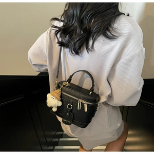 Close-up of black box-shaped crossbody bag with lychee texture and cute plush monster charm