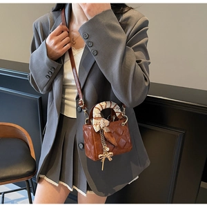 Detail of a brown quilted mini crossbody bag featuring a silk scarf handle and golden bow charm