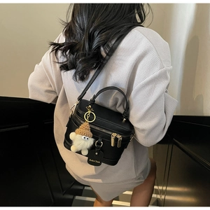 Detail of black pebbled leather mini box bag with gold zippers and fluffy white charm