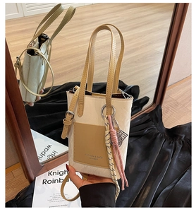 Detail view of cream bucket bag with khaki contrast pocket and woven rope tassel