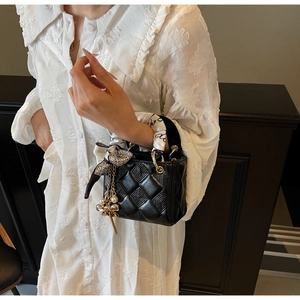 Close-up of black quilted handbag with scarf-wrapped handle and pearl bow pendant charm