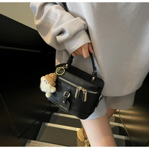 Detail of black lychee leather box bag with golden zipper and plush doll pendant