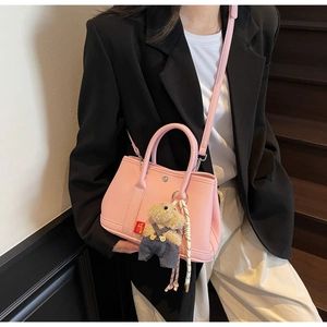 Sac seau rose grainé avec pendentif ourson porté sur un blazer noir décontracté