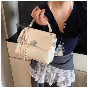 Detail of cream glossy tote bag with silver crescent buckle and decorative rope charm