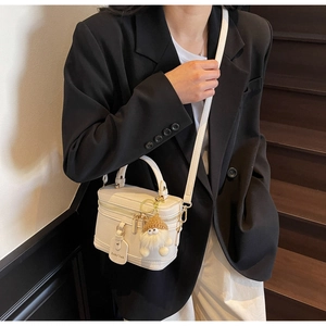 Close-up of a white lychee leather box bag featuring a plush gnome charm on the zipper