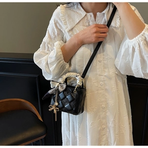 Detail of black quilted crossbody bag with silk scarf handle and golden bow charm