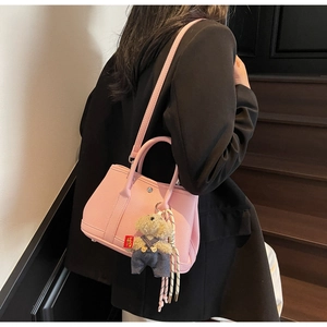 Détail du sac seau rose clair avec motif litchi et breloque ours sur un mannequin femme