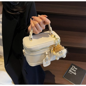 Detail of white vanity bag with lychee grain texture and cute plush monster charm