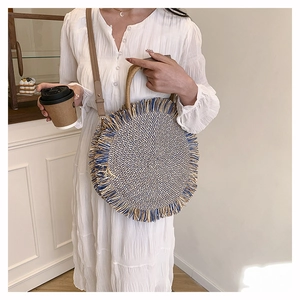 Close-up of circular woven straw bag with contrasting blue tassels and a leather strap