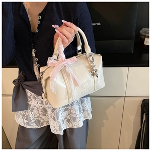 Close-up of cream Boston bag featuring lace ribbon bow and heart metal charms