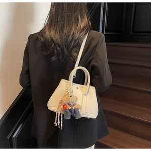 Détail du sac seau en cuir blanc avec breloque ours et pompon tissé coloré