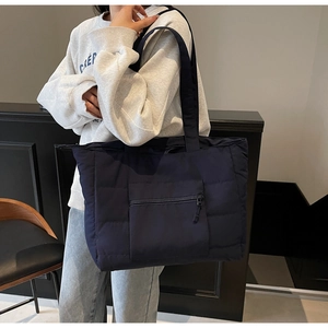Détail d'un grand cabas matelassé bleu marine avec poche zippée porté à l'épaule