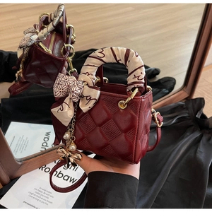 Detail of burgundy quilted leather handbag with silk scarf handle and pearl bow charm
