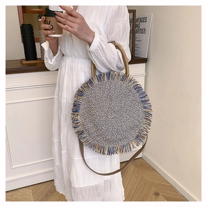 Detailed view of woven straw round handbag with tassels and long leather shoulder strap