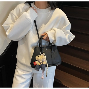 Détail du sac seau noir en cuir grainé avec un pendentif ours sur sweat blanc