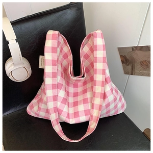 Close-up of pink checkered canvas tote bag with woven brand label on a leather surface