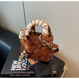 Close-up of brown quilted handbag with silk scarf handle and pearl butterfly charm on books