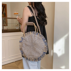 Close-up of a woven straw round bag with navy fringe tassels and brown leather strap