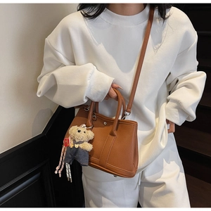 Vue détaillée du cuir marron à motif lychee et du pendentif ours sur le sac seau tendance