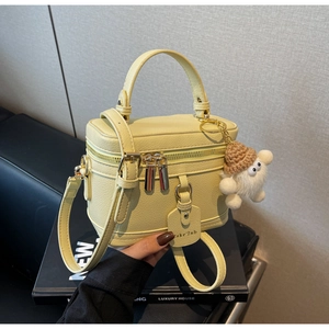 Detail of light yellow leather box bag with plush monster charm and top handle