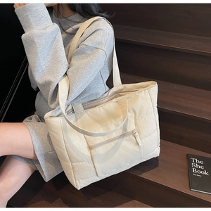 Détail d'un sac cabas matelassé beige avec poche zippée avant et texture en nylon doux