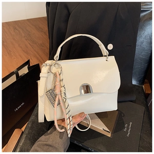 Detail of white leather tote bag featuring a metallic crescent lock and woven charm