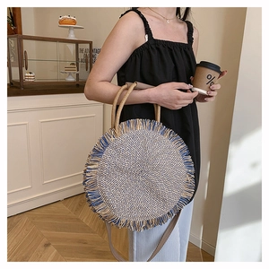 Detail of round woven straw bag with blue fringe tassels and leather shoulder strap