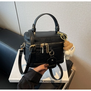 Close-up of black lychee grain leather box bag with a cute plush doll charm and gold zipper