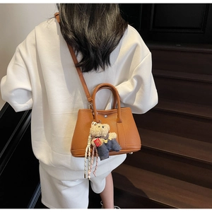 Détail du sac seau en cuir grainé marron avec breloque ours porté à l'épaule