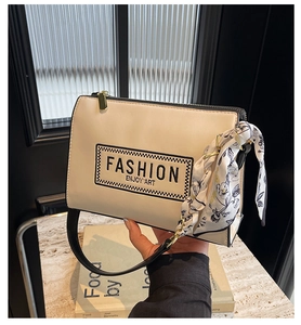 Detail view of beige crossbody bag with fashion embroidery, silk scarf, and gold hardware