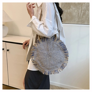 Detailed close-up of blue and beige woven straw round bag with fringe tassels and leather strap