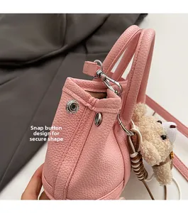 Detalle del bolso de cuero rosa con botón de presión lateral y colgante de oso