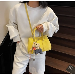 Détail d'un sac seau en cuir jaune avec breloque ours sur un escalier en bois