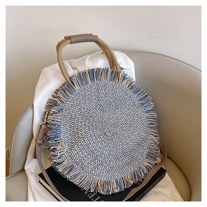 Detail of a round woven straw bag with blue and beige fibers and decorative fringe edges