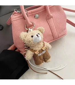 Primer plano de un colgante para bolso de oso de peluche beige con peto de pana café