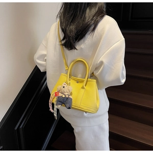 Détail du sac seau en cuir jaune avec breloque ours sur un escalier moderne