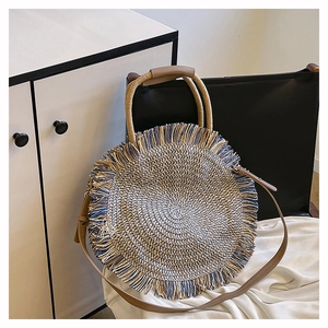 Detail of bohemian round straw bag with blue fringe trim and brown leather strap