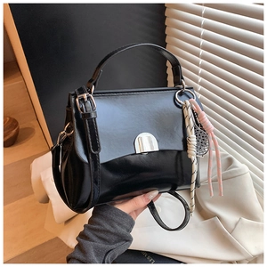 Detail of glossy black patent leather tote bag with silver metal clasp and woven charm