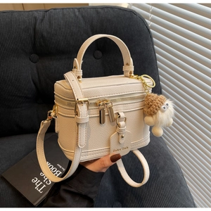 Detailed close-up of cream box bag in lychee leather with gold hardware and plush charm