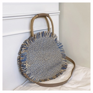 Detail of bohemian round woven straw bag with tassels and brown leather strap