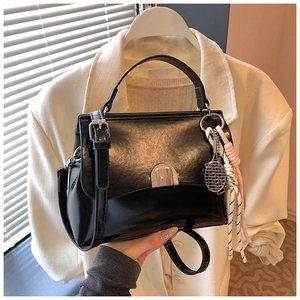 Detail of black glossy tote bag with silver buckle and tennis racket charm accessory