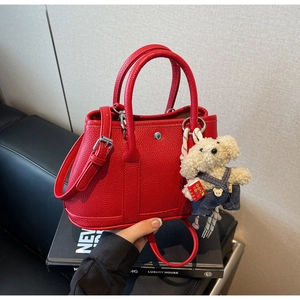 Gros plan d'un sac seau en cuir rouge avec boucle argentée et breloque chien en peluche
