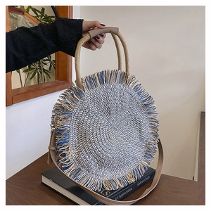 Close-up of bohemian woven round bag featuring beige and blue fringes and leather handle