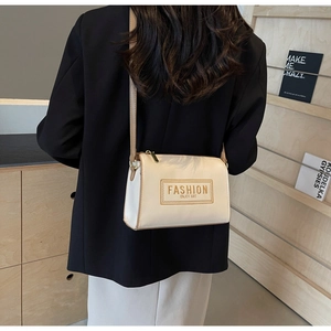 Detail view of cream crossbody bag with brown stitching on a model in a black blazer