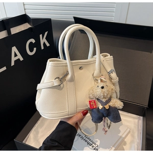 Détail d'un sac seau crème avec texture litchi et un charmant petit ours en peluche inclus